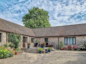 A stone building with a tiled roof, a staircase leading to a porch, and various potted plants.
