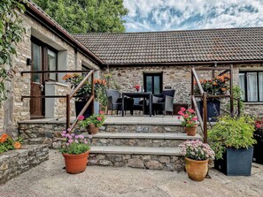A stone building with a tiled roof, outdoor seating area with chairs and tables, and potted plants.