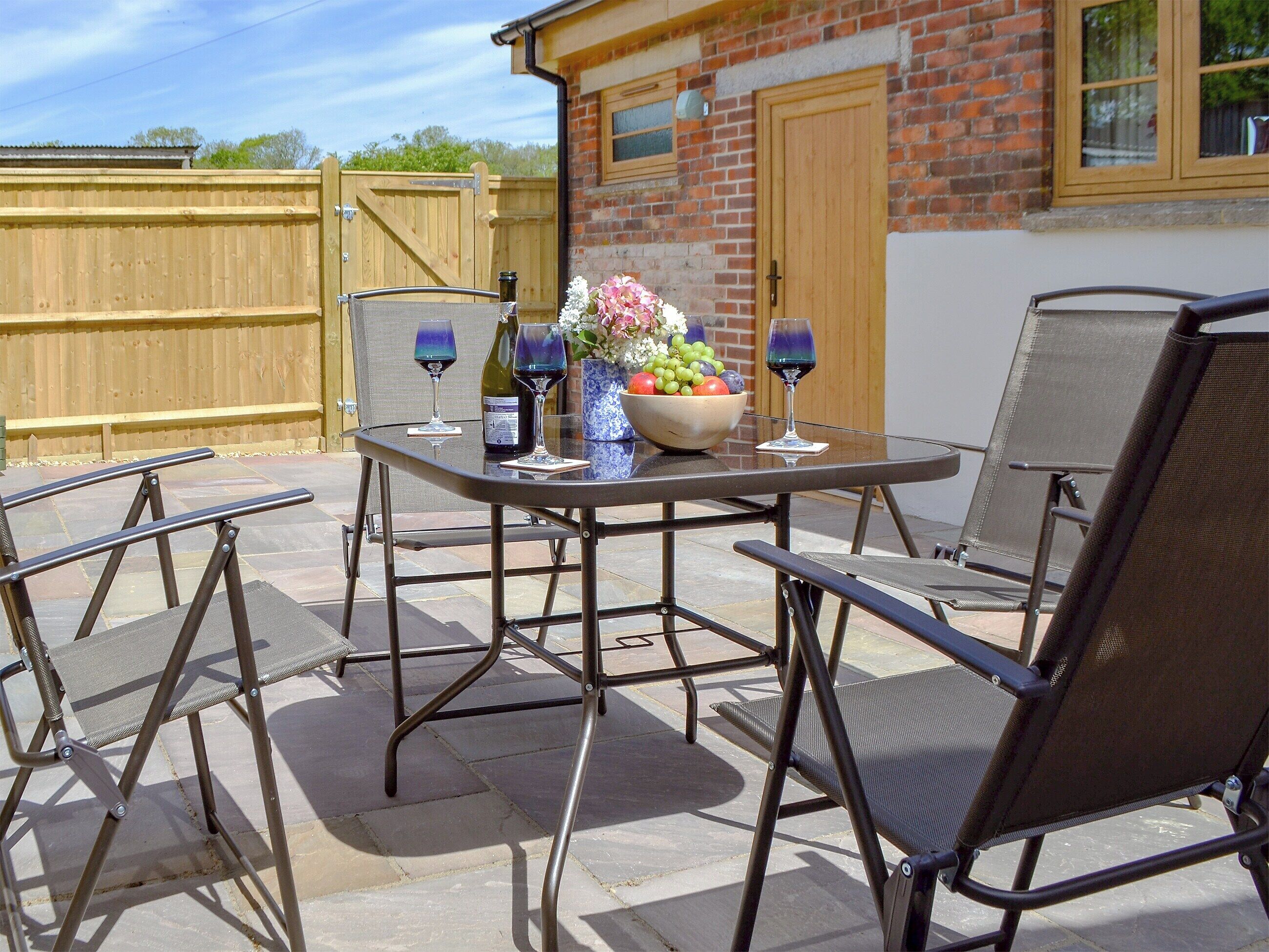 Une terrasse extérieure avec une table ronde, deux chaises et un vase rempli de fleurs.