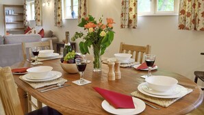A dining area with a wooden table set for a meal, surrounded by chairs. There are plates, glasses, and a vase with flowers on the table. - Woodlands Dairy Cottage (Adversane, near Billingshurst)