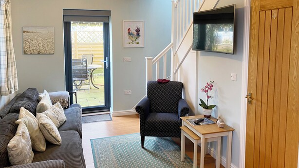 Una sala de estar con sofá, sillón, una mesita, televisor y escalera.