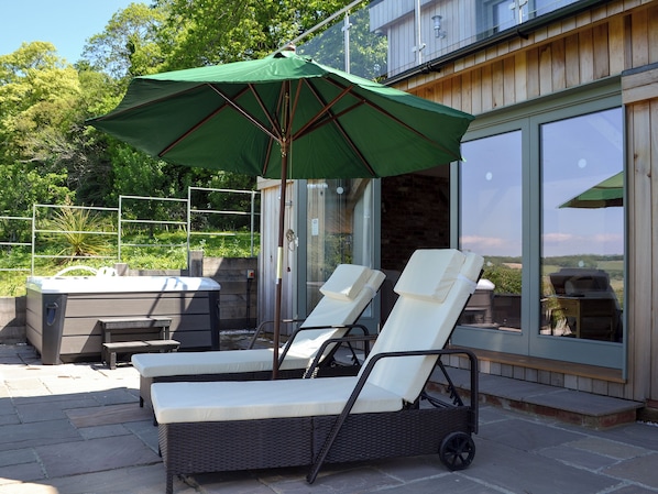 A patio area with two lounge chairs, a green umbrella, and a hot tub.
