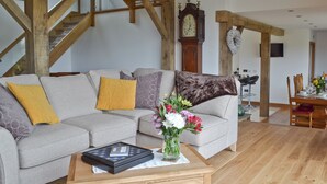 A living room with a grey sofa, wooden beams, a dining table with chairs, and a large wall clock. - 4 bedroom accommodation in Winchelsea, near Rye (Winchelsea, near Rye)
