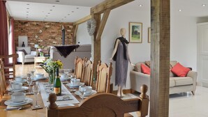 A dining area with a long wooden table set for a meal, a mannequin dressed in a dress, and a brick wall in the background. - 4 bedroom accommodation in Winchelsea, near Rye (Winchelsea, near Rye)