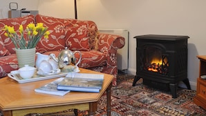A cozy living room with a sofa, a table with a teapot, a book, and a fireplace. - 2 bedroom accommodation in Kentmere, near Staveley (Kentmere, near Staveley)