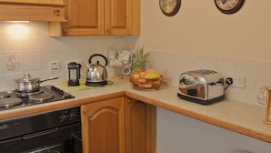 A kitchen with wooden cabinets, a stove, a kettle, a toaster, and a fruit bowl. - 2 bedroom accommodation in Kentmere, near Staveley (Kentmere, near Staveley)