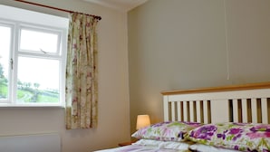 A bedroom with a bed, floral curtains, a bedside lamp, and a window with a view of a green landscape. - 2 bedroom accommodation in Kentmere, near Staveley (Kentmere, near Staveley)