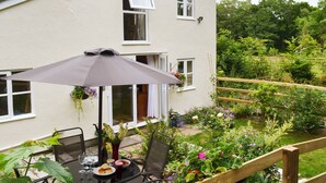 Eine Terrasse mit Esstisch, umgeben von üppiger Bepflanzung und einem Holzzaun.