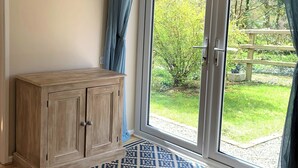 Ein Zimmer mit einem Holzkasten, einem gemusterten Teppich und einer Glastür, die in einen Garten führt.