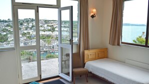 Quarto com cama, cadeira, janela com vista para uma cidade e porta que dá para o exterior.