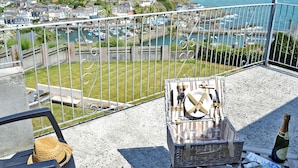 Varanda com vista para uma vila costeira, uma cesta de vime, uma garrafa e um chapéu.