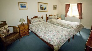 A bedroom with two single beds, a wooden dresser, a wicker chair, and a window with curtains.