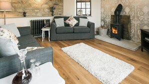A cozy living room with a stone wall, a fireplace, a grey sofa, and a white rug. - 2 bedroom accommodation in Alton, near Chesterfield (Alton, near Chesterfield)