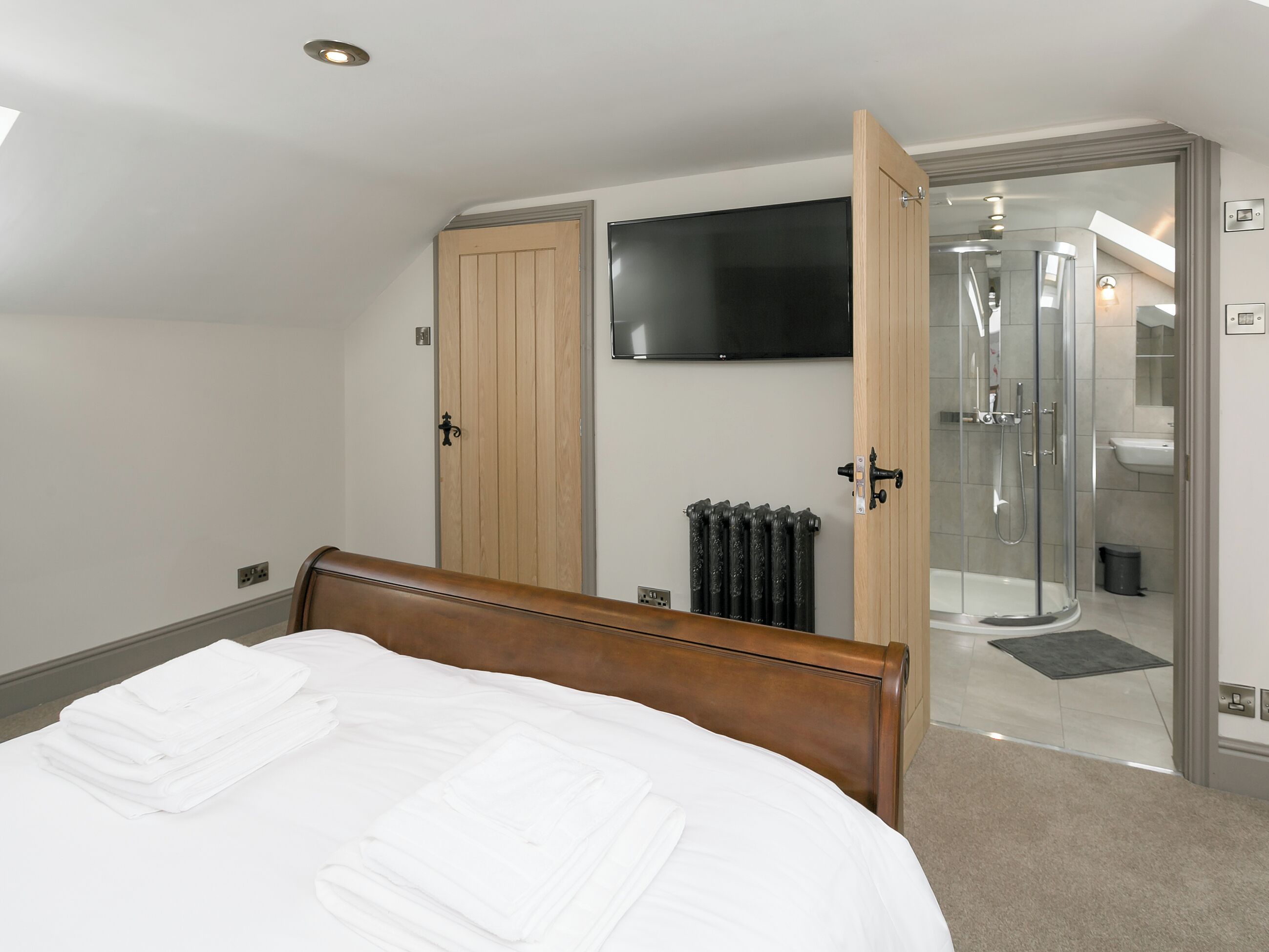 Habitación de hotel con cama, televisor montado en la pared, zona de ducha y puerta de acceso al baño.