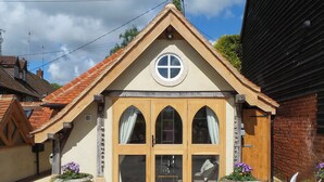 A building with a gabled roof, a central circular window, and a set of wooden double doors. There are two outdoor tables and chairs, and flower planters are visible. - 1 bedroom accommodation in Turville, near Henley-on-Thames (Turville, near Henley-on-Thames)