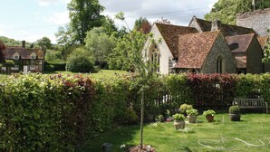 A traditional stone building with a steeply pitched roof, surrounded by lush greenery and a well-maintained garden. - 1 bedroom accommodation in Turville, near Henley-on-Thames (Turville, near Henley-on-Thames)