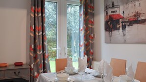 Comedor con una mesa para cuatro, una estantería y una ventana con cortinas.