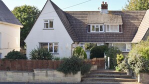 Una casa de dos pisos con techo a dos aguas, una chimenea visible y una entrada frontal con escalones.