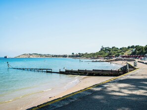 Une plage côtière avec une jetée qui s’avance dans l’eau, un rivage sablonneux et, en arrière-plan, des collines.