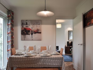 Un comedor con una mesa preparada para cuatro personas, un cuadro en la pared y un pasillo que conduce a otra habitación.