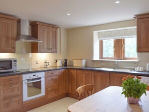 A kitchen with wooden cabinets, a microwave, an oven, a coffee maker, and a window with a view of trees.