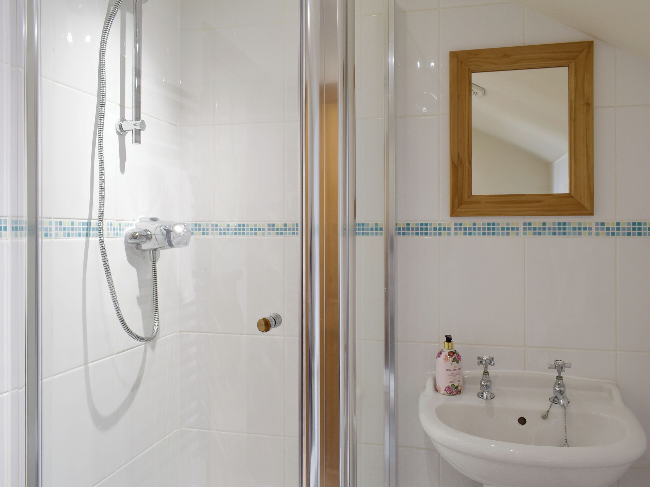Un baño con cabina de ducha de vidrio, un lavamanos con espejo de marco de madera y salpicadero de azulejos.