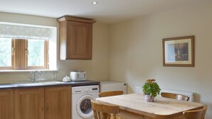 Une cuisine avec des meubles de rangement en bois, un lave-linge, un grille-pain et une table à manger avec des chaises.