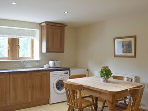A kitchen with wooden cabinets, a washing machine, a toaster, and a dining table with chairs.