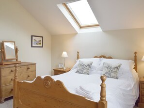 A bedroom with a sloped ceiling, a skylight, a wooden bed with white bedding, a nightstand with a lamp, and a dresser with a mirror. - The Old Dairy - UKC3413 (Bolton-by-Bowland)
