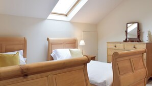 Une chambre avec un puits de lumière, deux lits en bois, une commode et un miroir.
