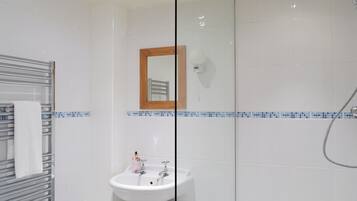 A bathroom with a glass shower enclosure, a white sink, and a towel rack.