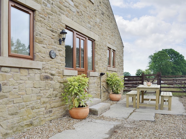 A stone building with a wooden door and windows, a small outdoor seating area with a table and chairs, and two potted plants.