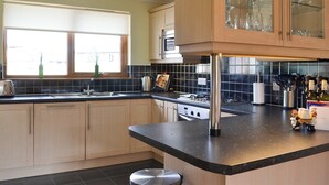 Una cocina moderna con armarios de madera, encimera negra y un mueble superior con puerta de vidrio.