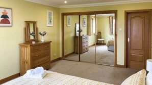Un dormitorio con cama, cómoda, espejo y una puerta que da a otra habitación.