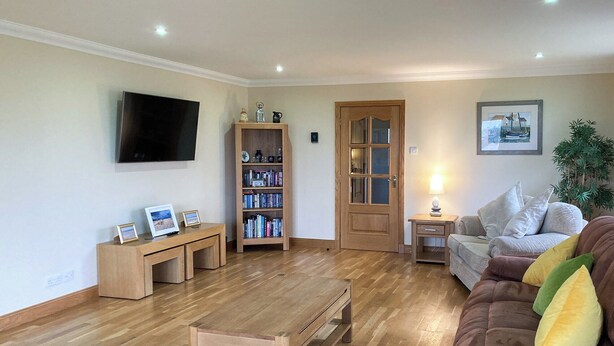 Una sala de estar con una mesa de centro de madera, un sofá de cuero marrón, una estantería y un televisor montado en la pared.