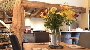 A wooden dining table with a vase of yellow flowers, a wooden chair, and a kitchen in the background. - 2 bedroom accommodation in Shobley, Ringwood (Shobley, Ringwood)
