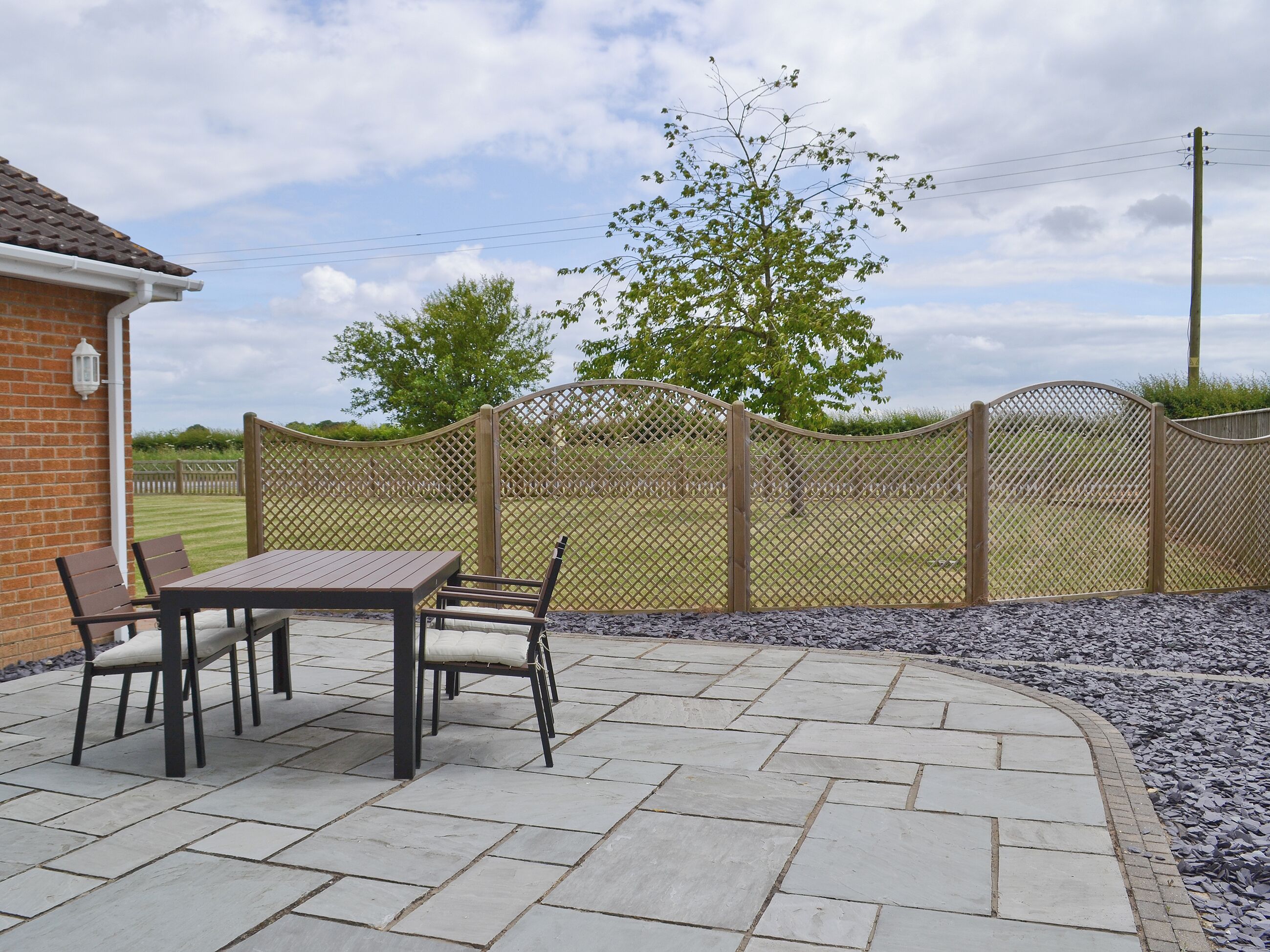 Une terrasse avec une table et des chaises, un mur en briques et une clôture offrant une vue sur un champ verdoyant.