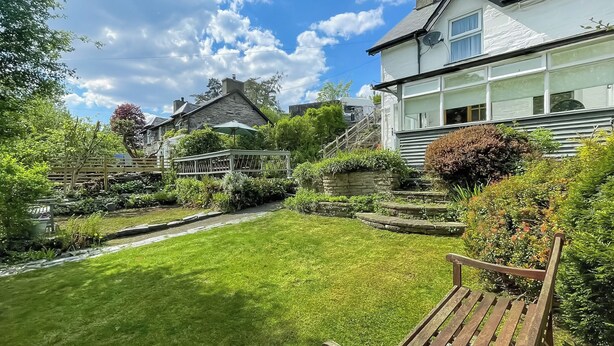 Un jardin bien entretenu, avec un banc en bois, un chemin de pierres et un bâtiment blanc doté de grandes fenêtres.