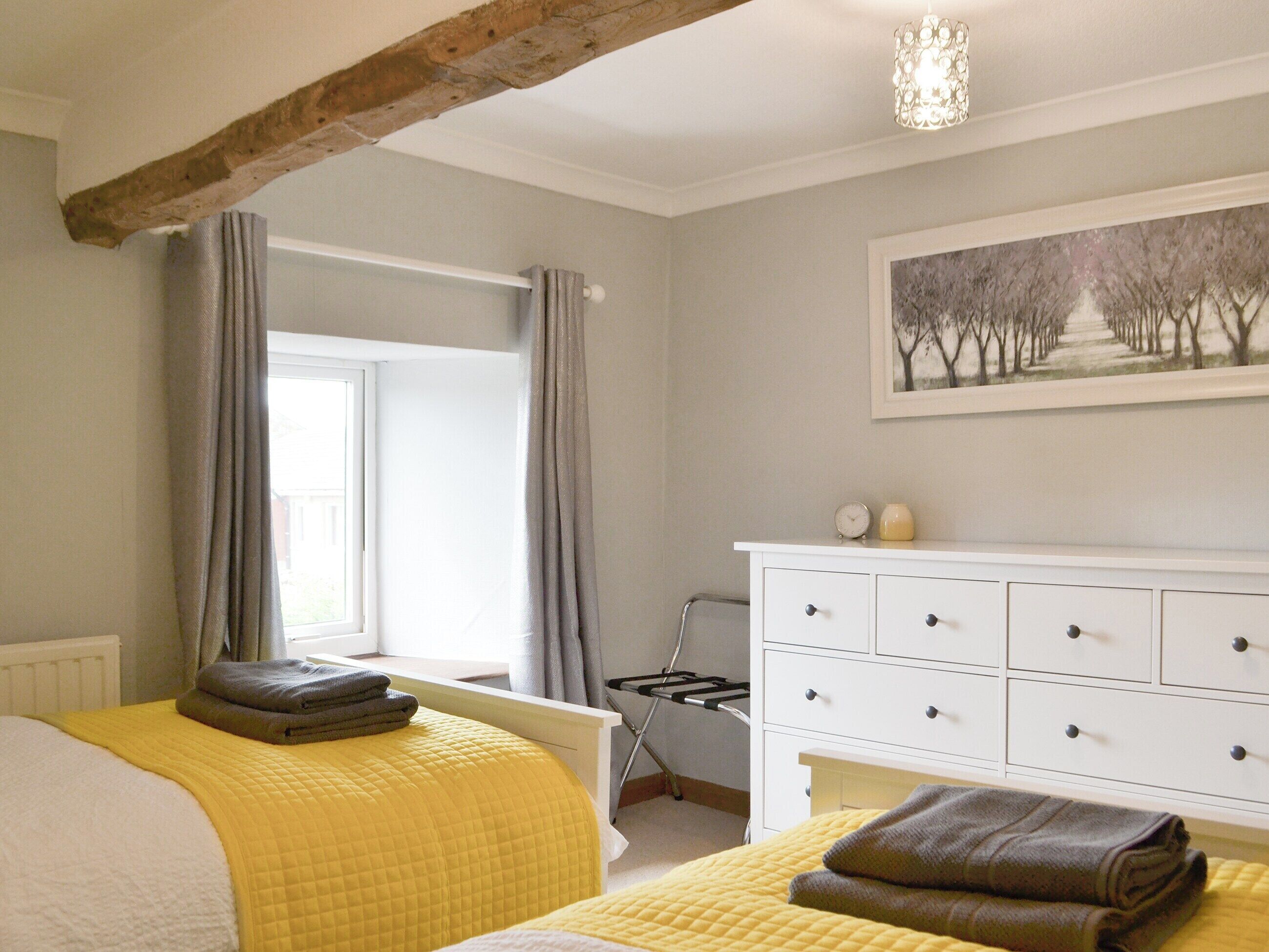 A bedroom with a bed, a dresser, a radiator, a window with curtains, and a painting on the wall.