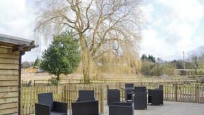 An outdoor patio area with wicker furniture, a wooden fence, and a large tree. - 1 bedroom accommodation in Six Ashes, near Bridgnorth (Six Ashes, near Bridgnorth)
