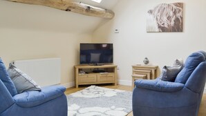 A cozy living room with a television, two blue armchairs, a wooden cabinet, and a ceiling with exposed beams and skylights. - 1 bedroom accommodation in Six Ashes, near Bridgnorth (Six Ashes, near Bridgnorth)