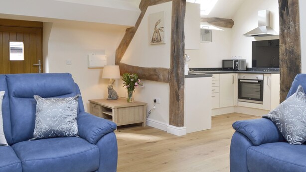 A modern living room with two blue sofas, a wooden floor, a kitchen with white cabinets, and exposed wooden beams. - 1 bedroom accommodation in Six Ashes, near Bridgnorth (Six Ashes, near Bridgnorth)