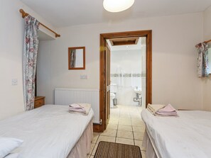 Une chambre avec deux lits, un radiateur, un miroir et une salle de bain visible à travers une porte ouverte.