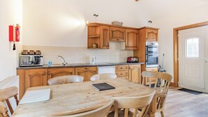 Cocina con armarios de madera, una mesa de comedor y sillas. Hay un microondas, un tostador y un horno.