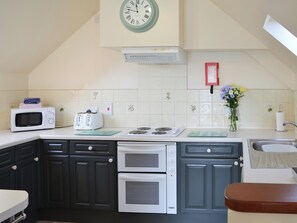 Una cocina con armarios oscuros, un microondas, un tostador, una estufa y un reloj en la pared.