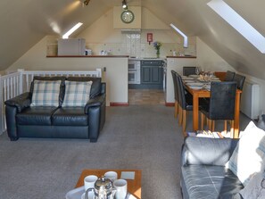 A cozy loft-style living space with a dining area, kitchenette, and a black leather sofa with plaid cushions.