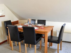 A dining table set for six with black chairs, a vase with dried flowers, and a framed picture on the wall. - 2 bedroom accommodation in Stalham (Stalham)