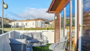 Un patio con mobiliario exterior, una puerta corrediza de vidrio y vista a casas móviles al fondo.