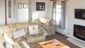 Una sala de estar con un sofá, sillones, una mesa de centro de madera, chimenea y televisor.
