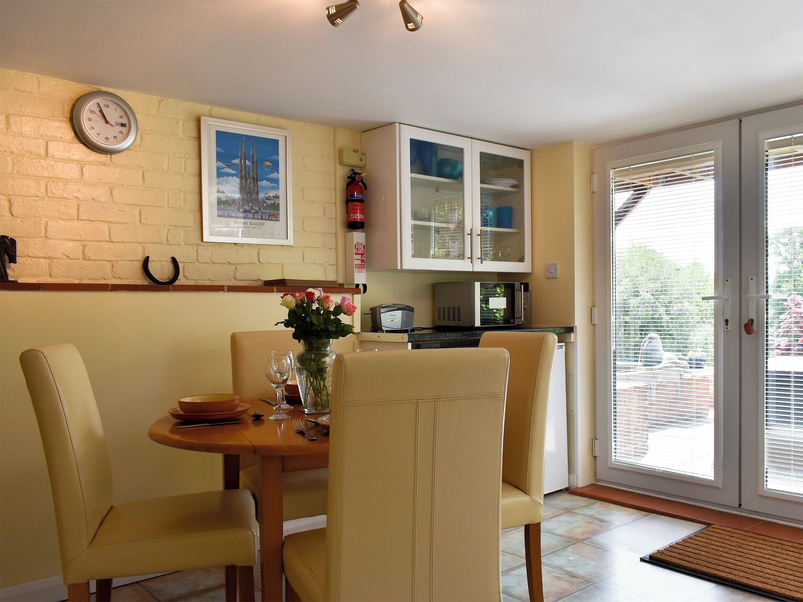 A dining area with a brick wall, a clock, a framed picture, and a cabinet with glass doors.